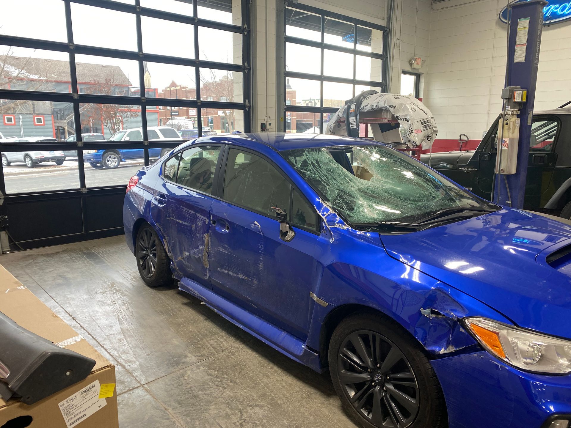 A blue car with a damaged windshield is parked in a garage.