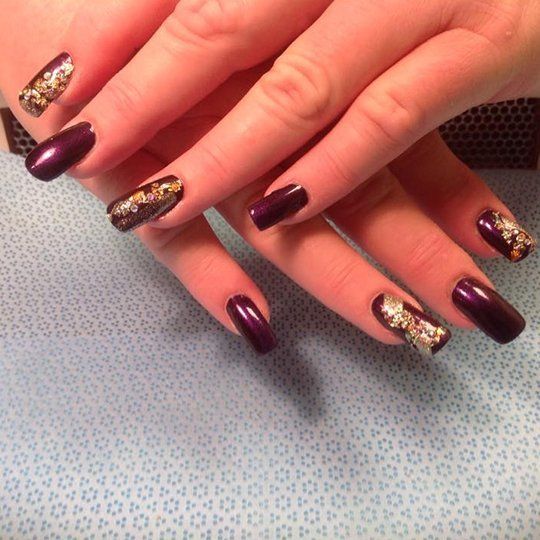 Hands with dark purple nail polish, two nails with gold foil design, on a blue surface.