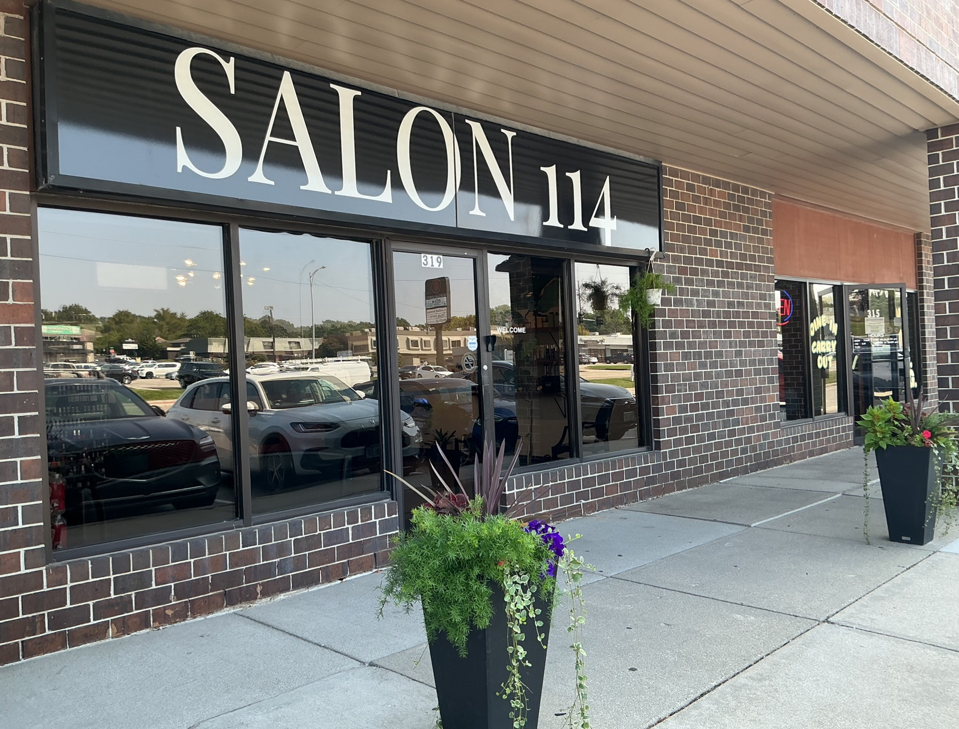 Salon 114 storefront with large windows, sign, and potted plants. Brick exterior.