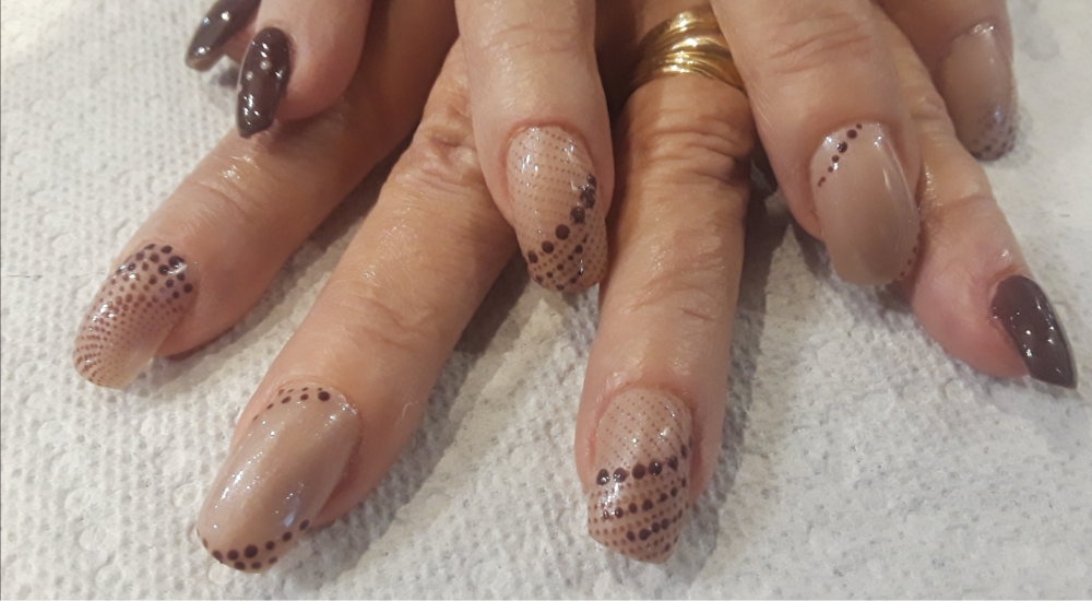 Hands with almond-shaped nails, some beige, some dark brown. Beige nails have dark dot designs.