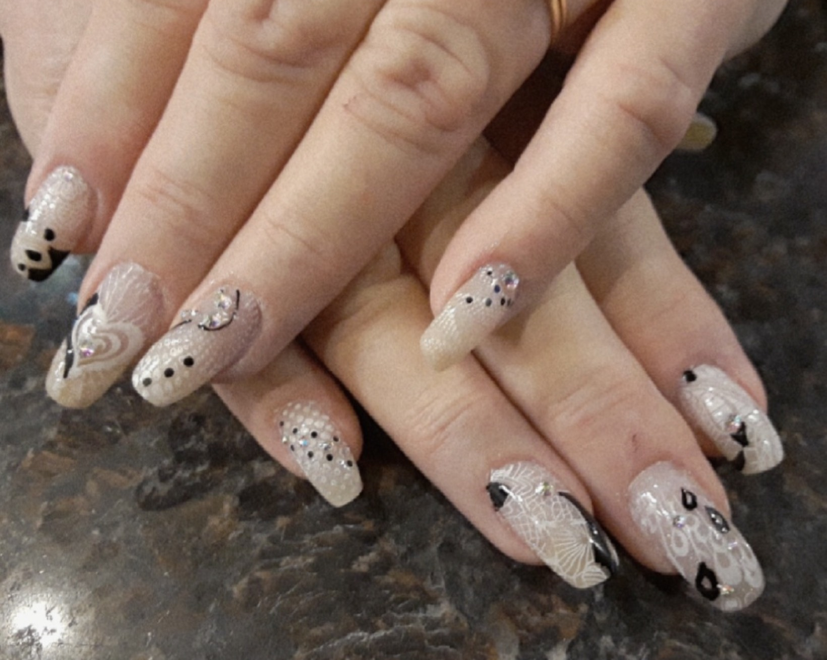 Hands with decorated nails: white, black, and silver designs on a neutral background.