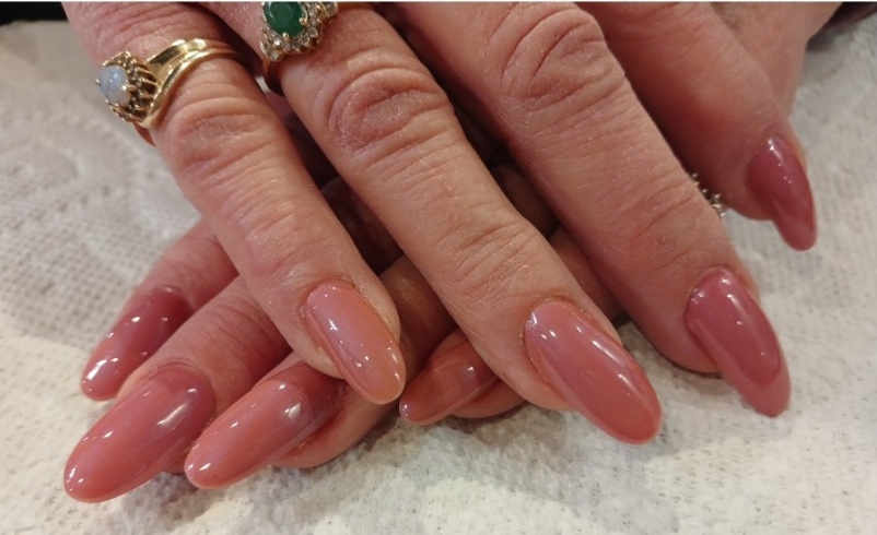 Hands with long, almond-shaped nails painted a light pink. Rings adorn some fingers.
