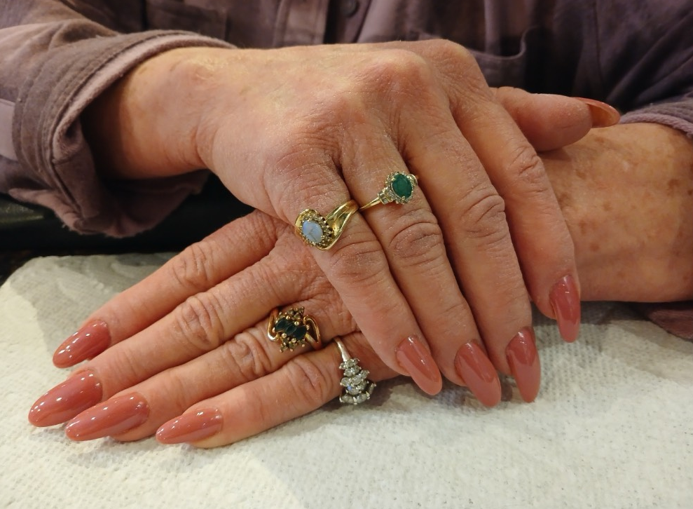 Hands with long, pink nails crossed, adorned with gold rings.
