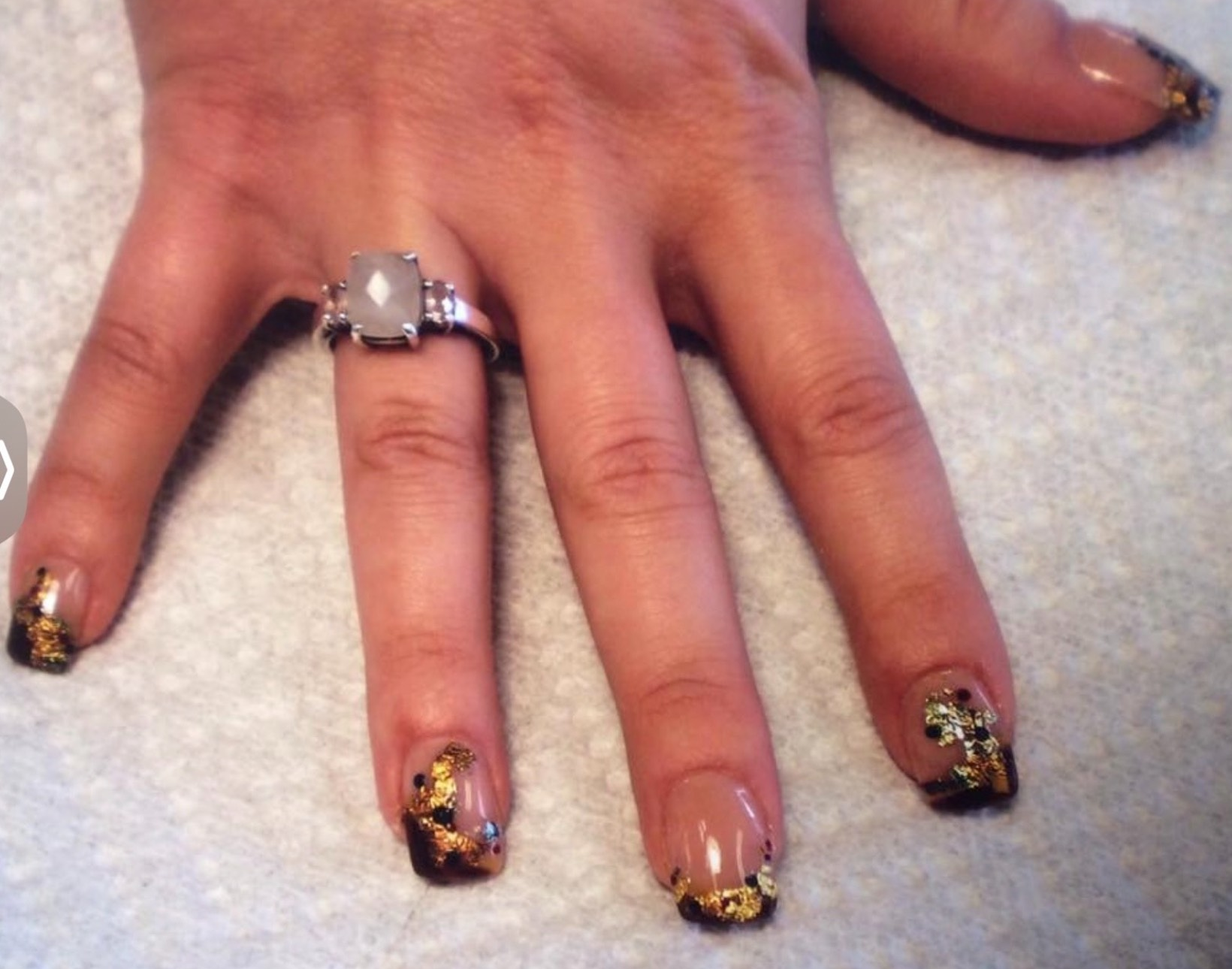 Hand with French manicure, gold foil detail on tips; ring on finger.