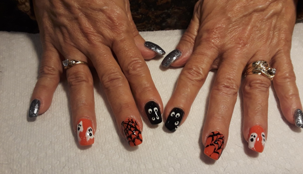 Hands with Halloween-themed nail art: orange and black nails with ghost and spider web designs.
