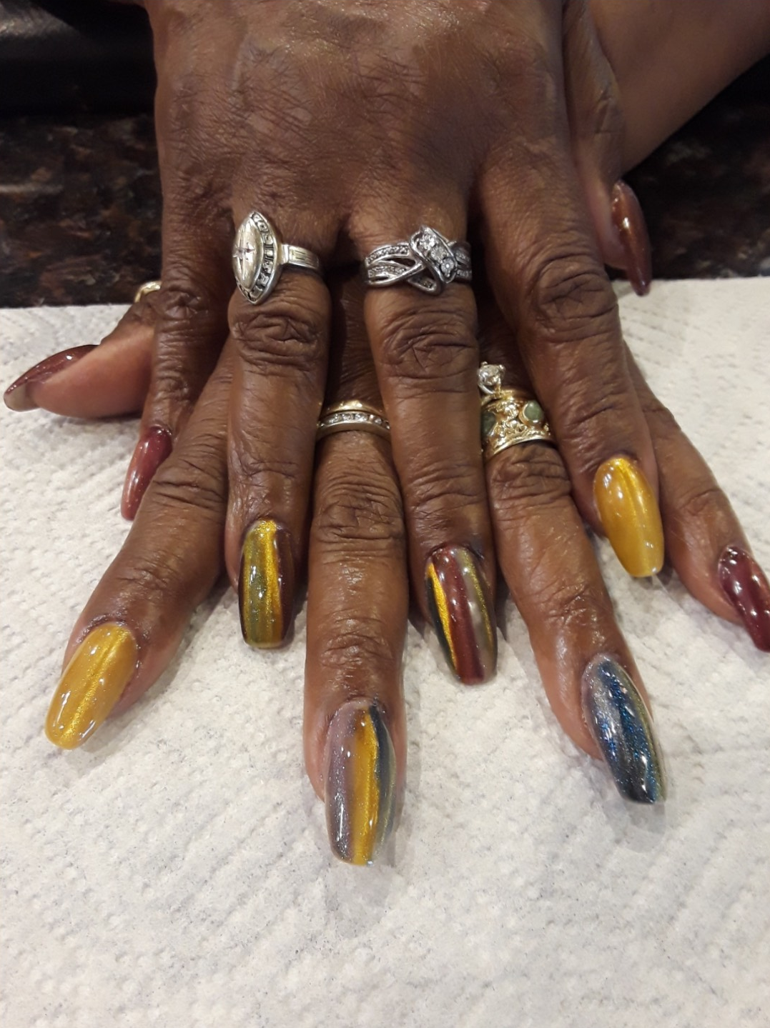 Hands with long, colorful, and artistic nail designs, adorned with several rings.
