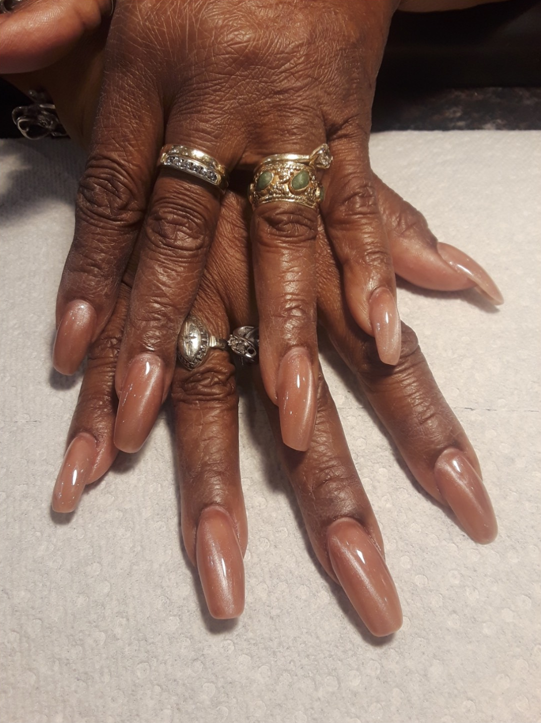 Hands with long, glossy, taupe-colored nails; wearing rings.