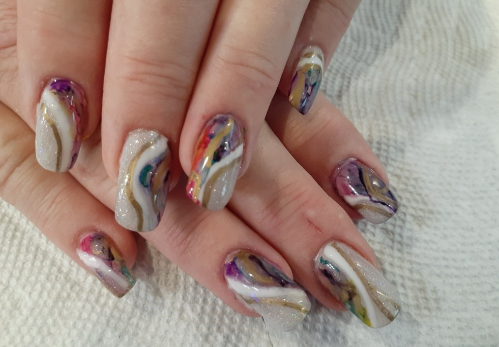Hands with marble-design nail polish in beige, gold, purple, red, and green.