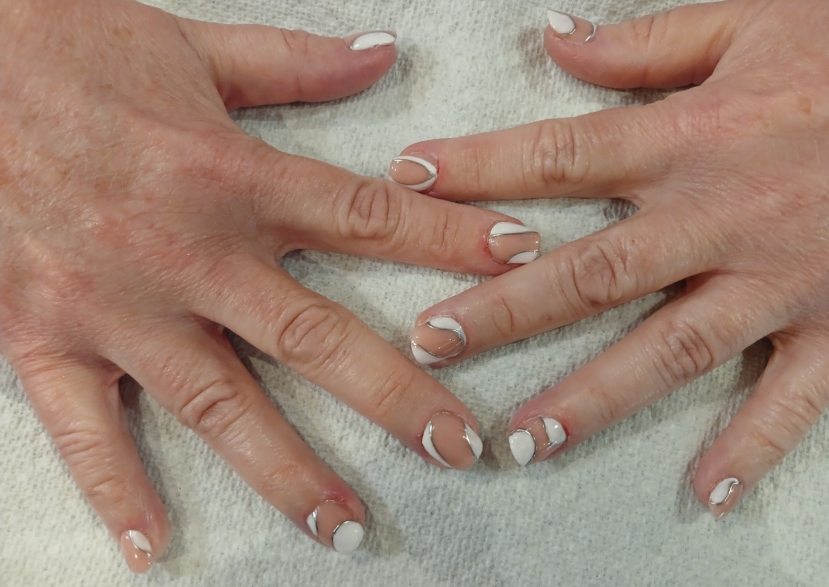 Hands with white-tipped nails arranged on a white towel.