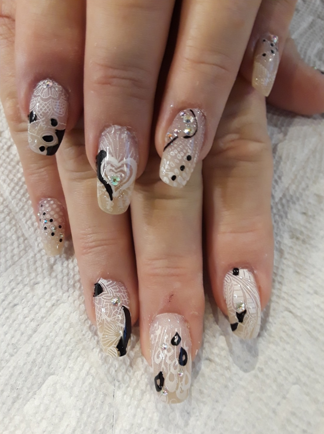 Close-up of hands with elegant, glittery nail art in neutral tones with black accents.