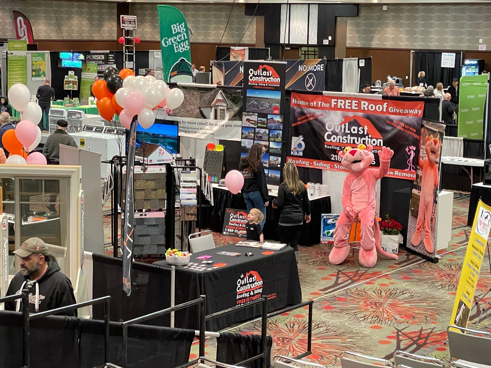 A pink panther mascot is standing in a room at a convention.