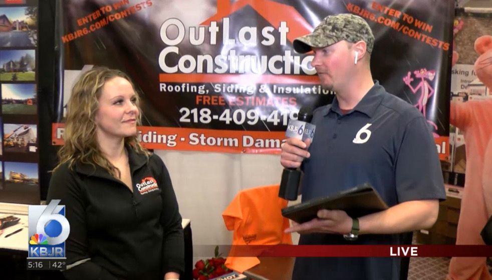 A man and woman are talking in front of a sign that says outlast construction