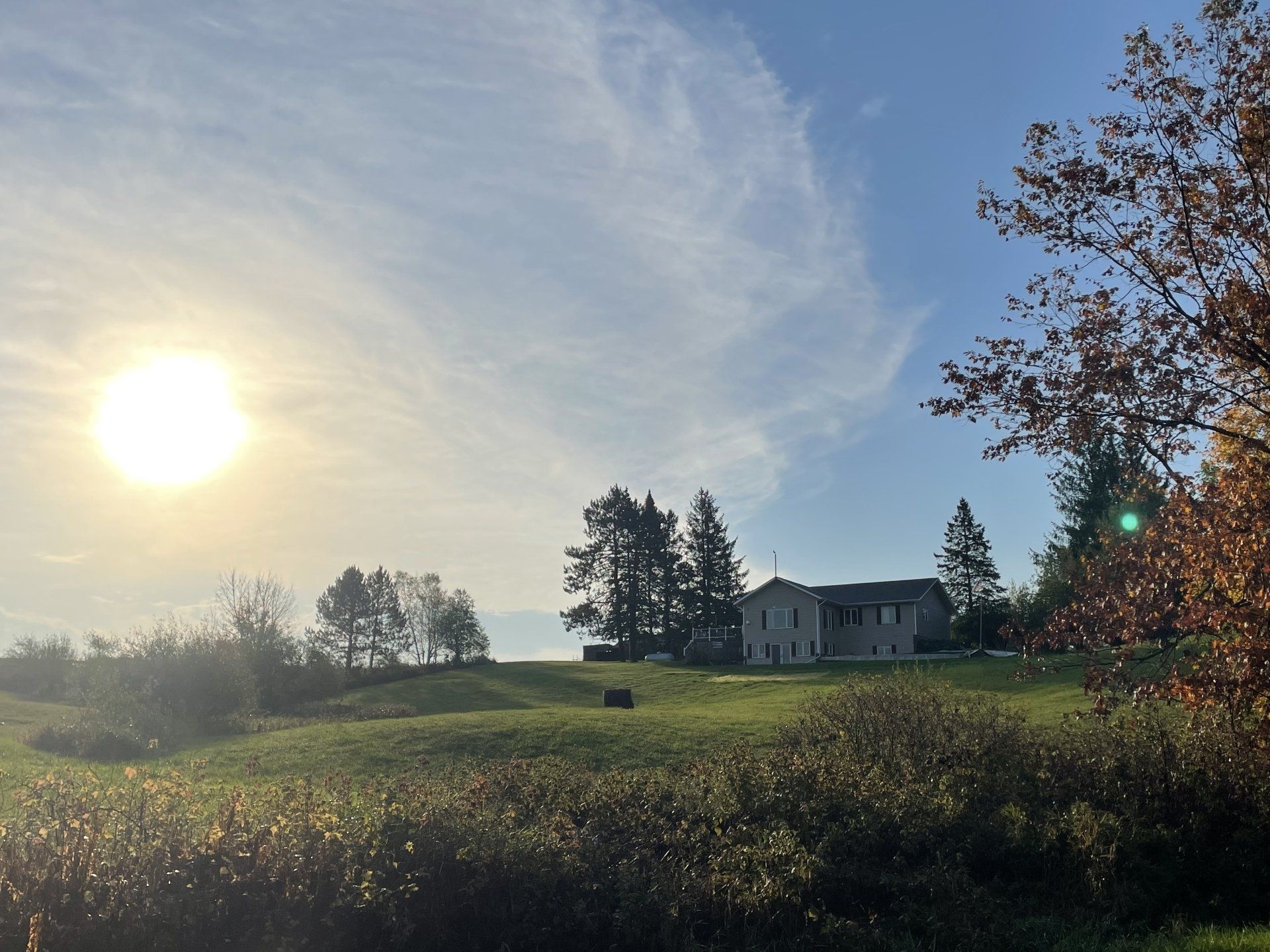 The sun is shining brightly over a field with a house in the background