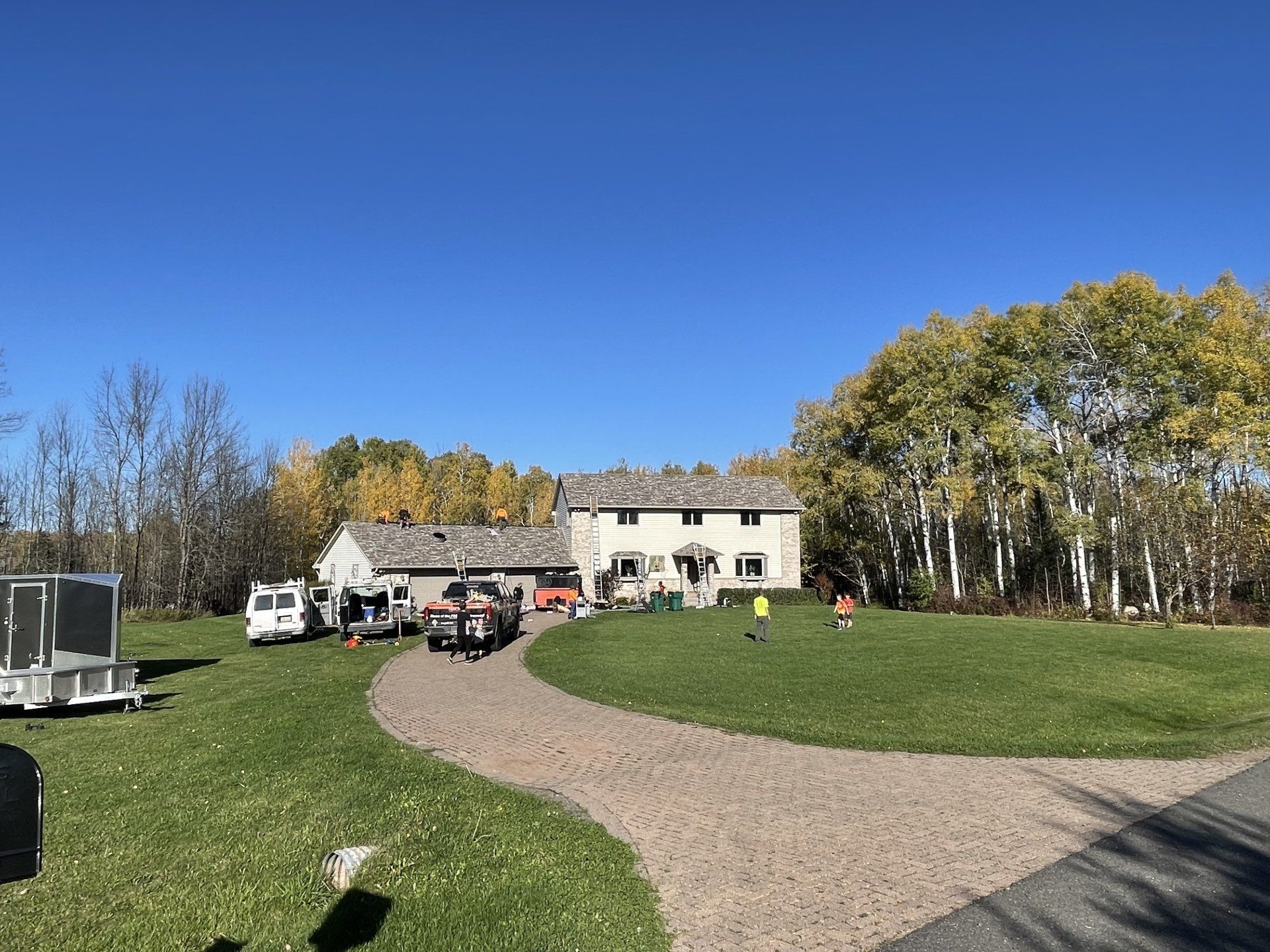 A large house is sitting on top of a lush green field next to a gravel driveway.