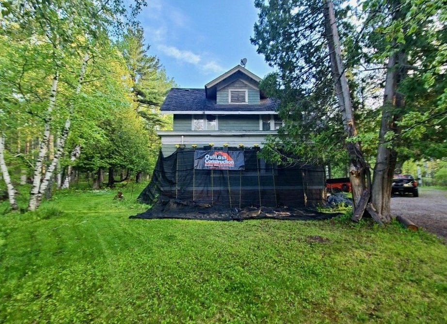 A large house is sitting in the middle of a lush green field surrounded by trees.