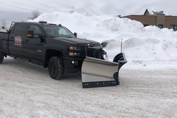 Black pickup truck with a snowplow parked on an icy road beside high snowbanks.