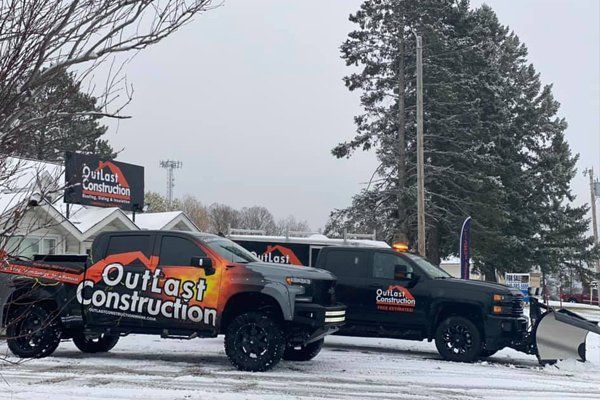 Two Outlast Construction trucks parked in a snowy lot with orange flame graphics and a plow attached.