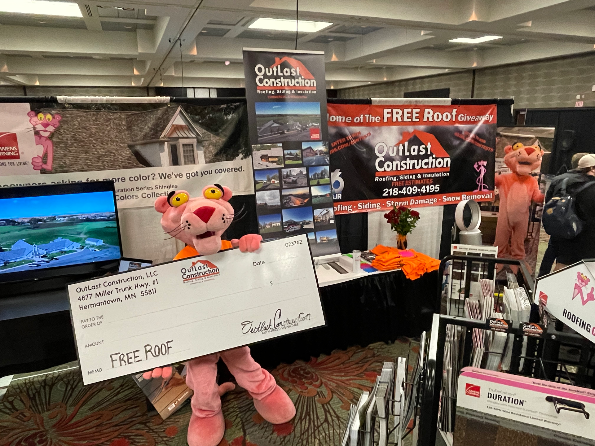A pink panther mascot is holding a large check at a convention.