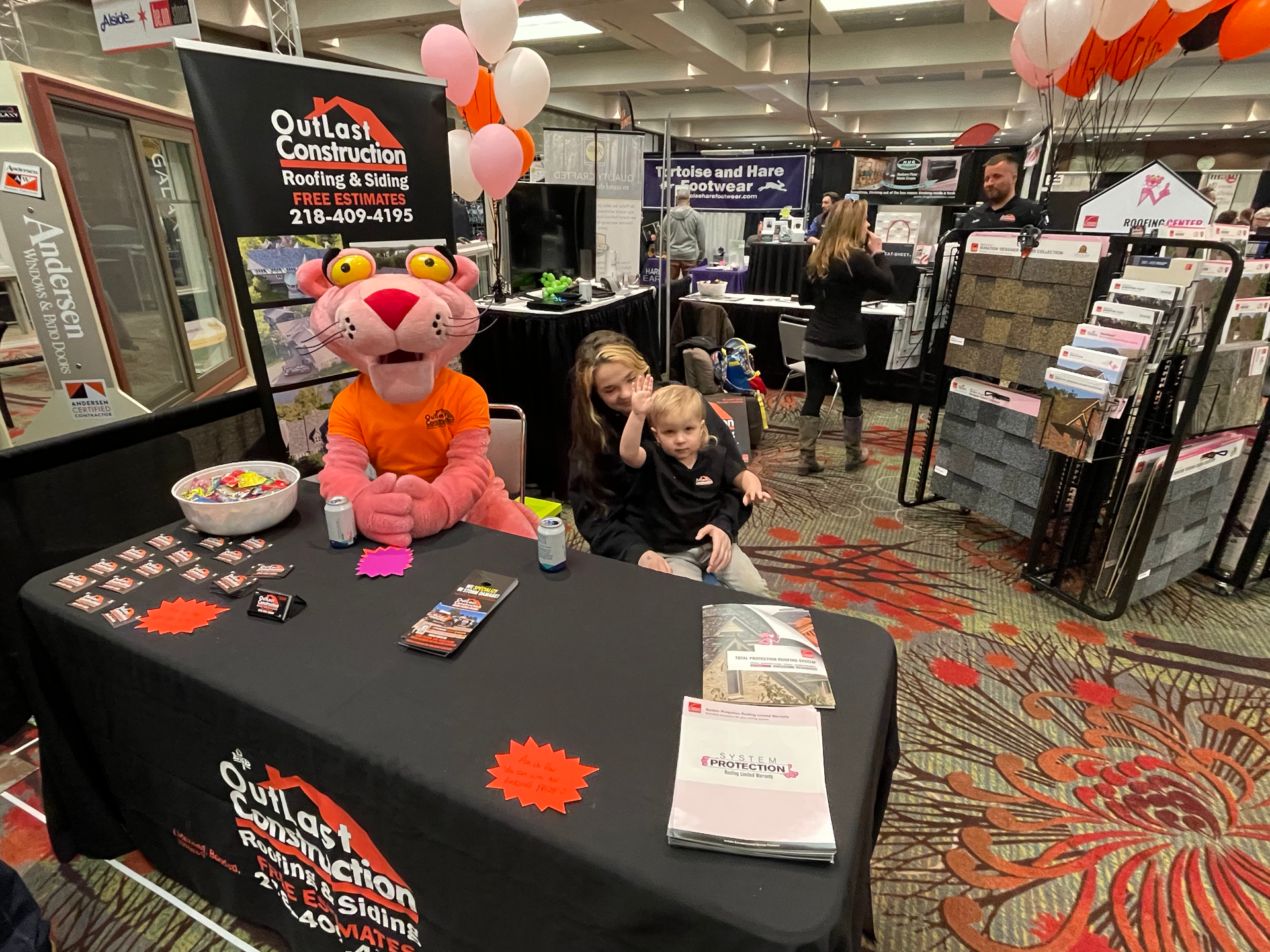 A pink panther mascot is sitting at a table with two children.