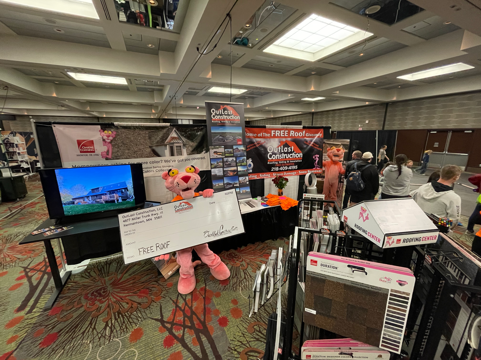 A pink panther mascot is standing in a room holding a check.