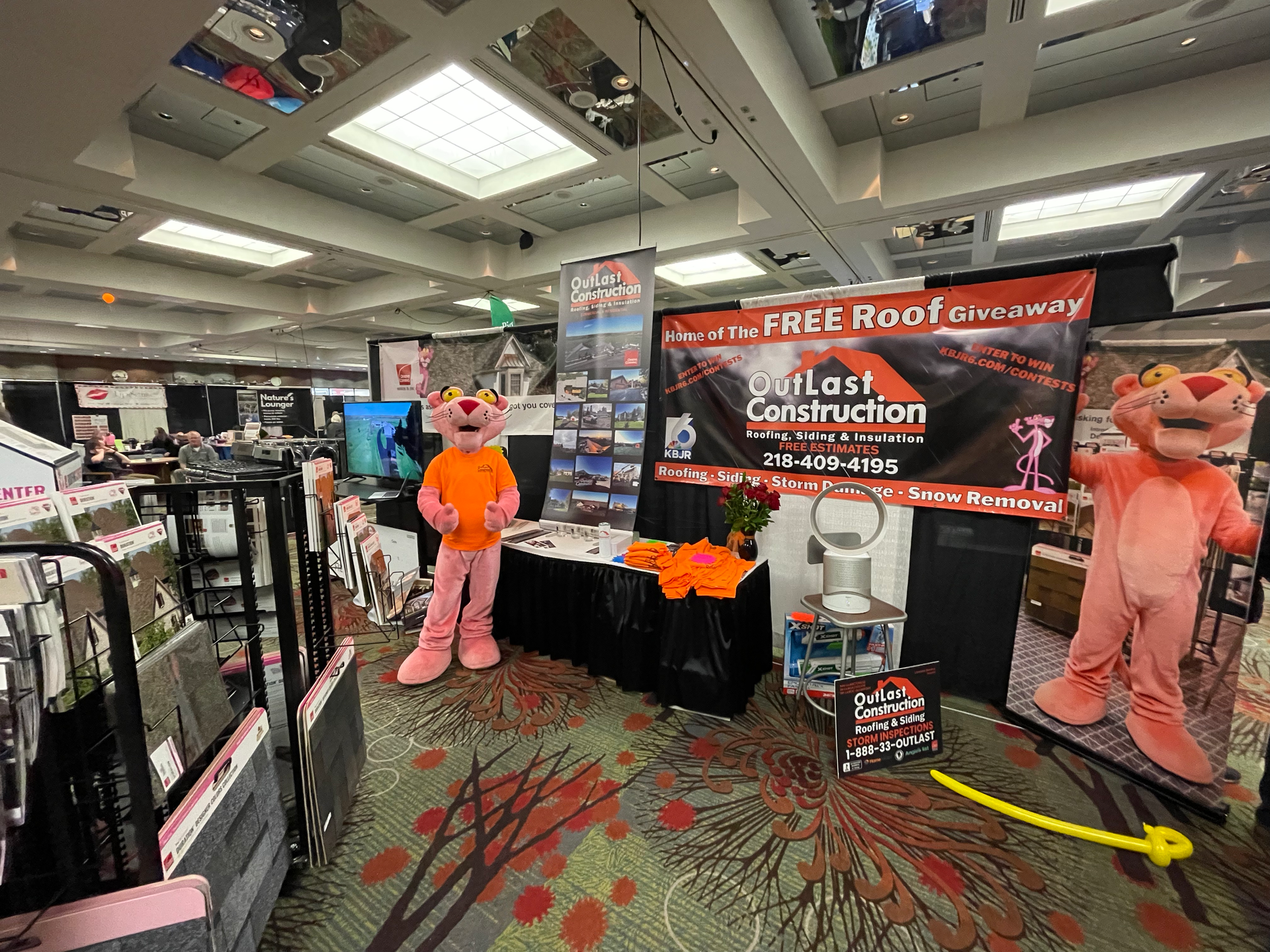 A pink panther mascot is standing in front of a sign that says `` free roof ''.