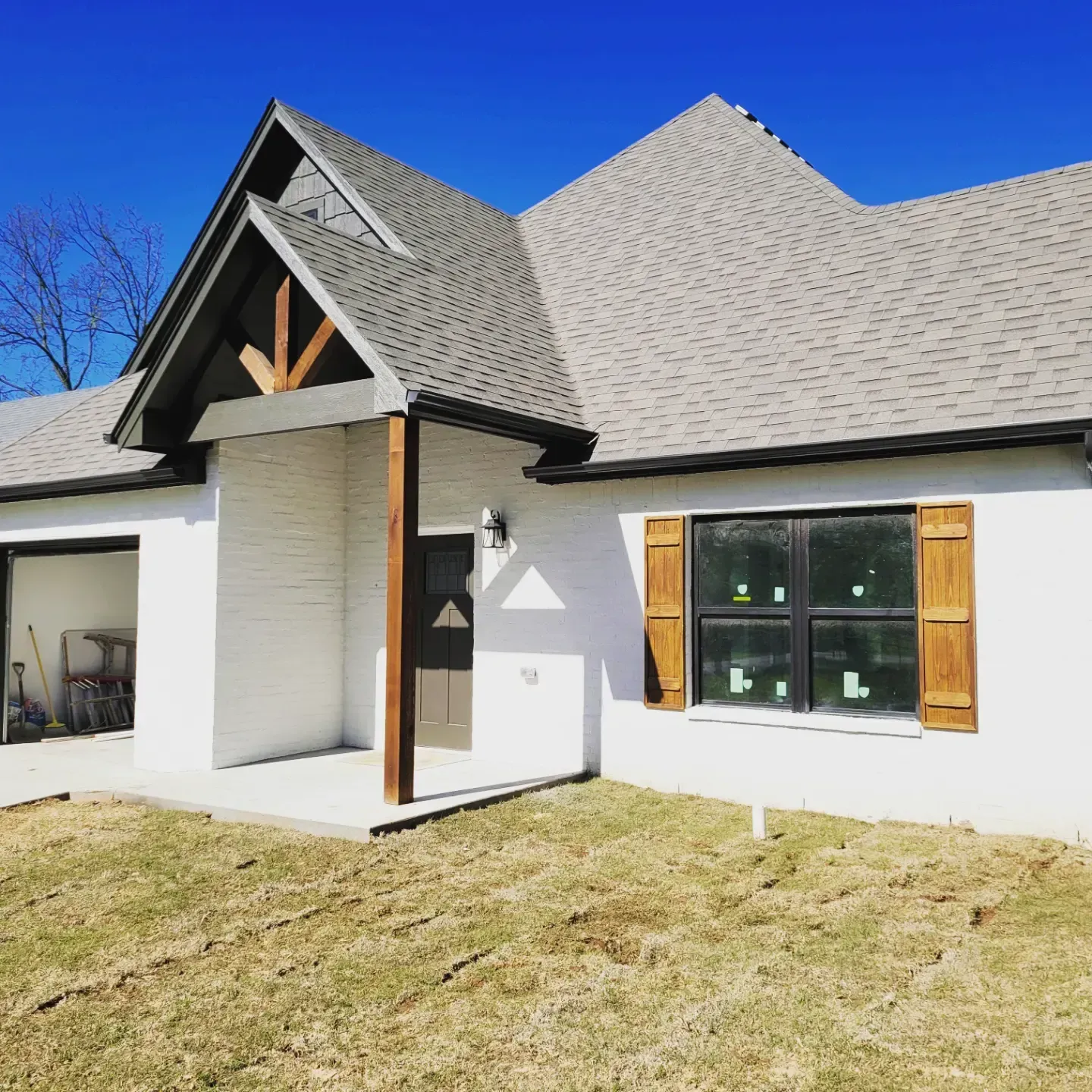 A single-story white brick house with a dark gabled roof, wooden entryway accents, and wooden window shutters.