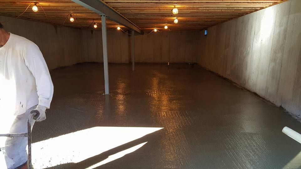 Newly poured concrete floor in a basement, with a person and overhead lighting.