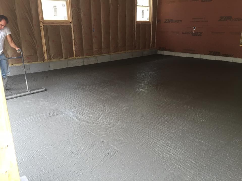 Man smoothing wet concrete floor with a long-handled tool in a partially constructed building.