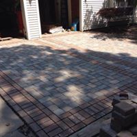 Brick paved driveway with brown border, in front of garage.