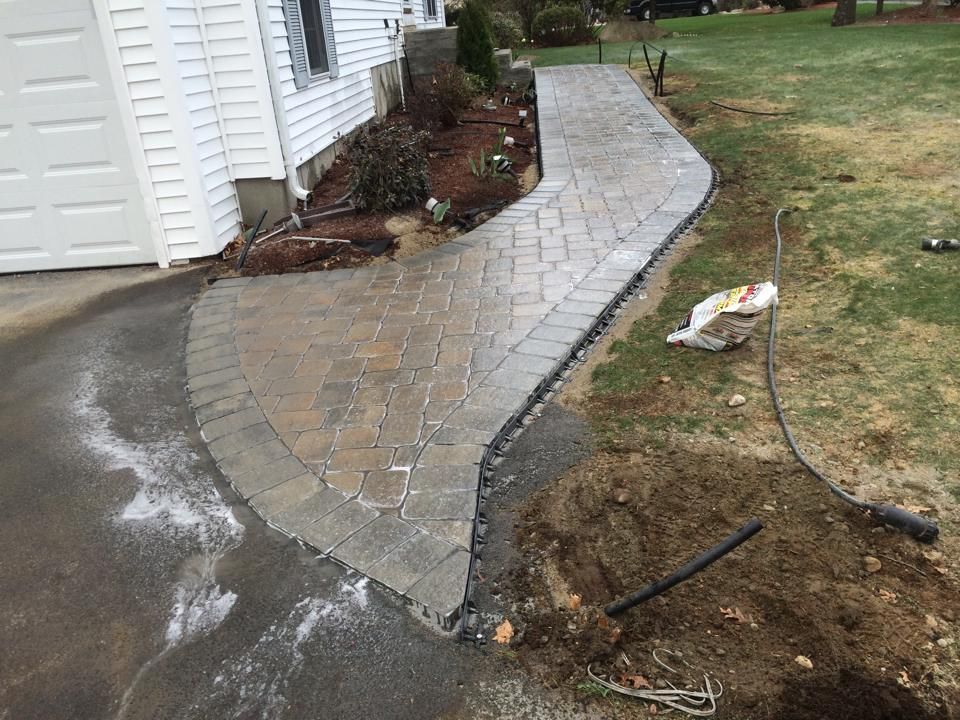Brick paved walkway curving from a driveway to a house, edged with dark border stones.