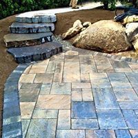 Stone steps leading to a patio with various-colored pavers; large boulders on the side.
