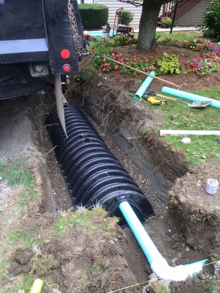 A black corrugated pipe is being installed in a trench. A truck and blue PVC pipes are also present.