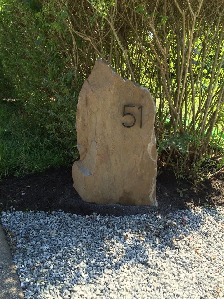 A large stone with the number 51 embedded, placed near shrubbery and gravel.