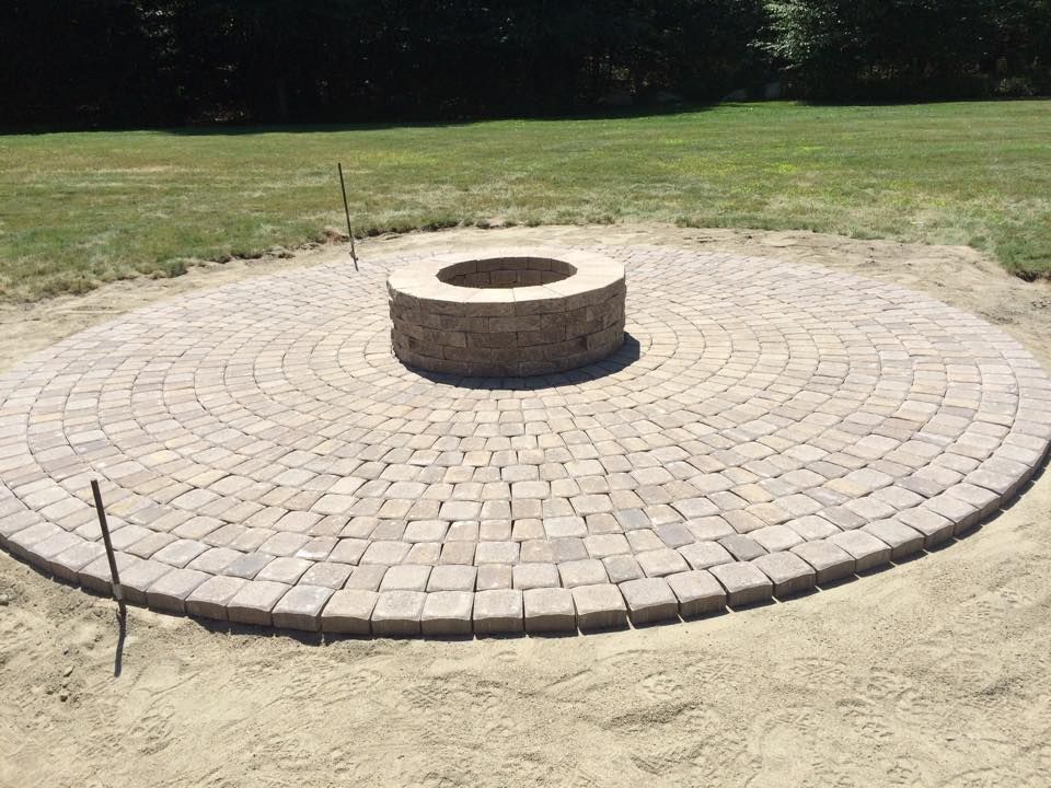 Circular brick patio with a central stone fire pit, on sand, outdoors.