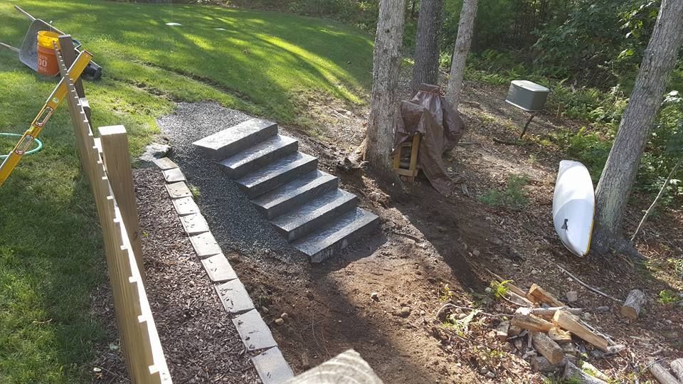 Stone steps leading up a slope, bordered by retaining wall and trees; construction materials present.