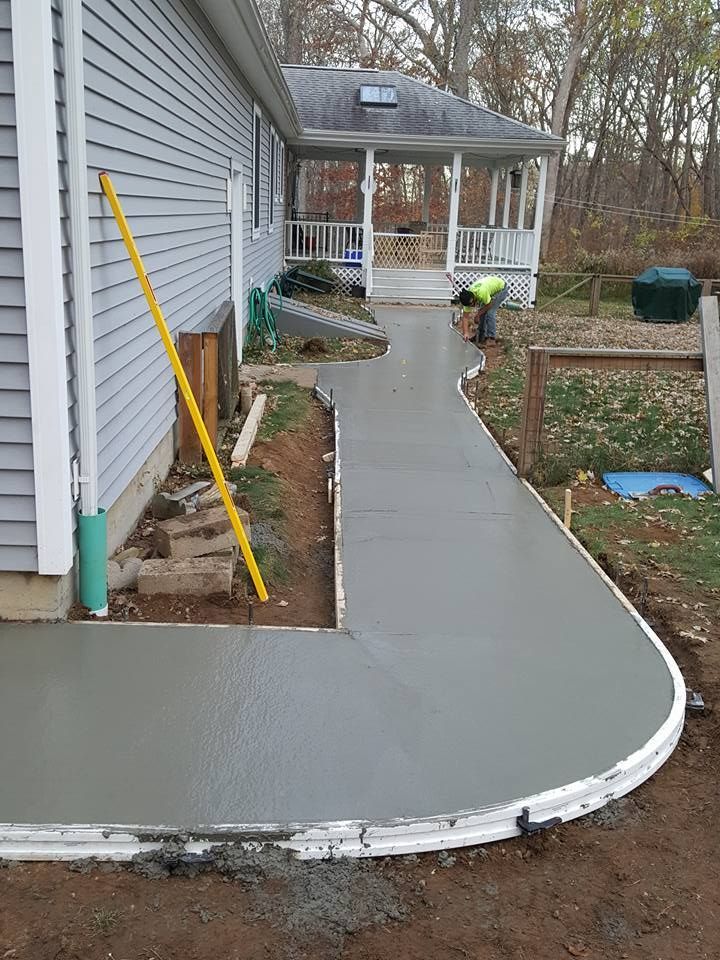 Freshly poured concrete walkway curves beside a house. A worker is visible.