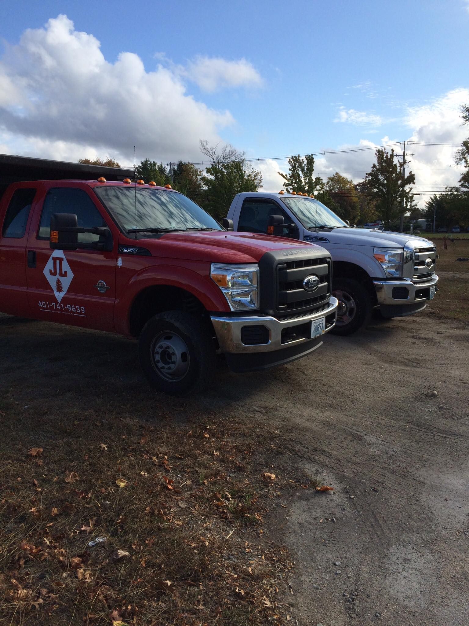 Two work trucks, one red and one white, parked outdoors under a cloudy blue sky.