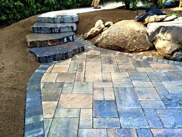 Stone patio with steps leading up, next to large boulders and a gravel area.