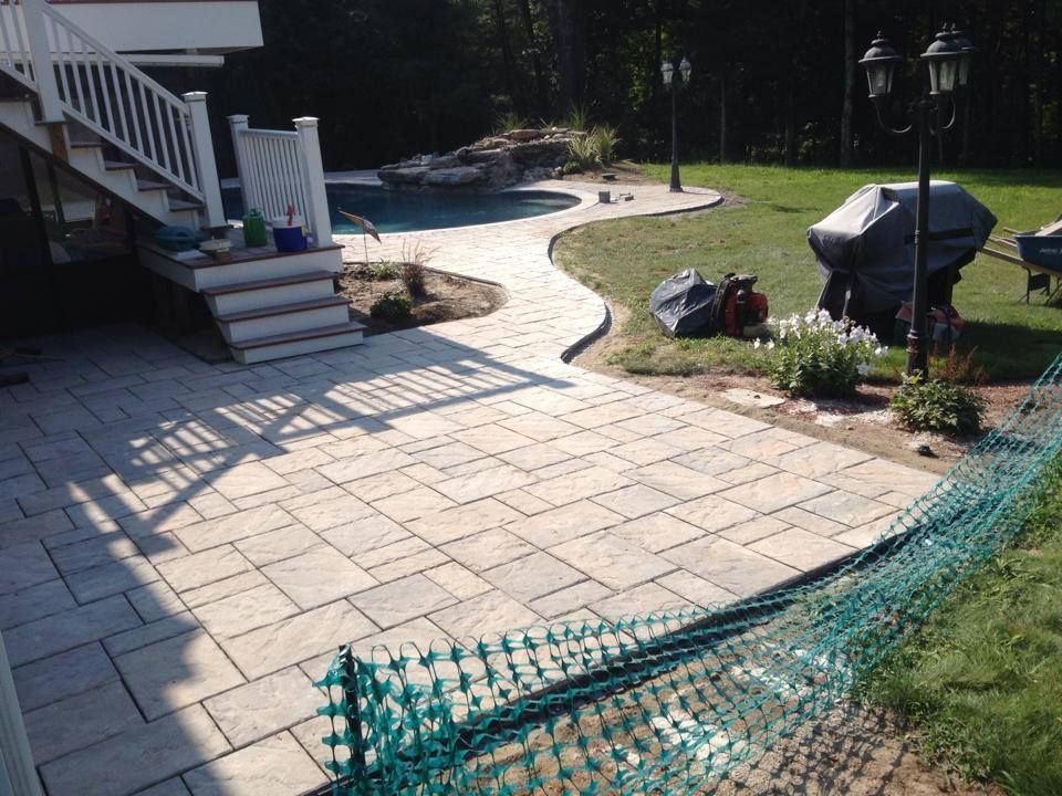 Stone patio with a curved walkway leading to a pool area and a covered grill.
