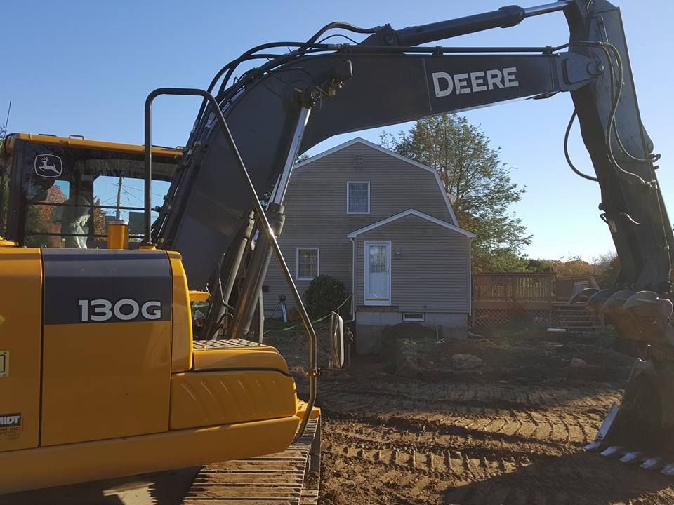 Yellow Deere excavator in front of a gray house.