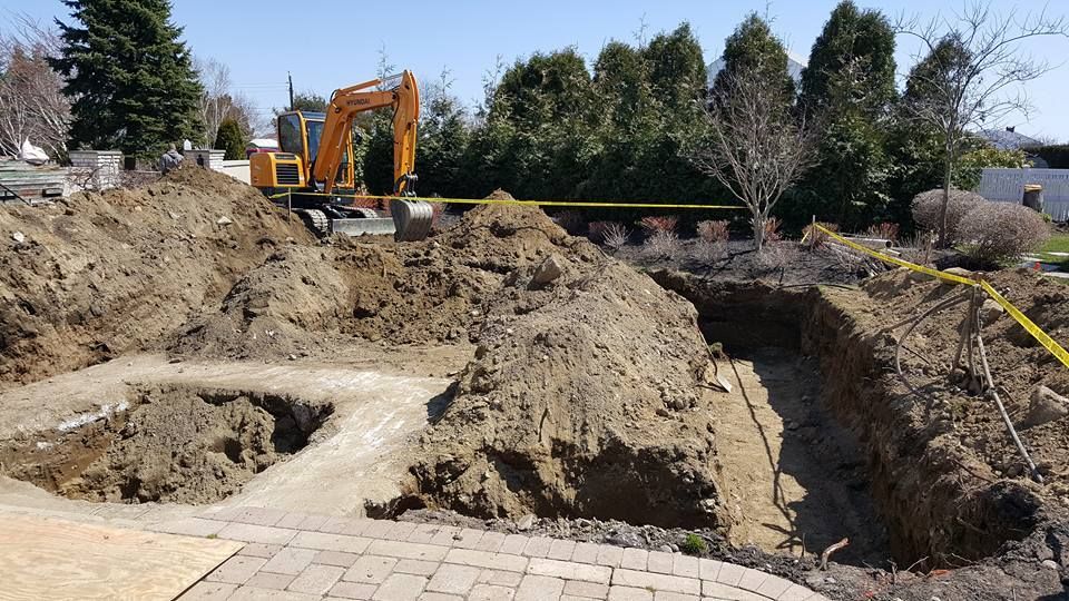 Excavation in progress; yellow excavator in a large dirt pit. Yellow caution tape in a residential yard.