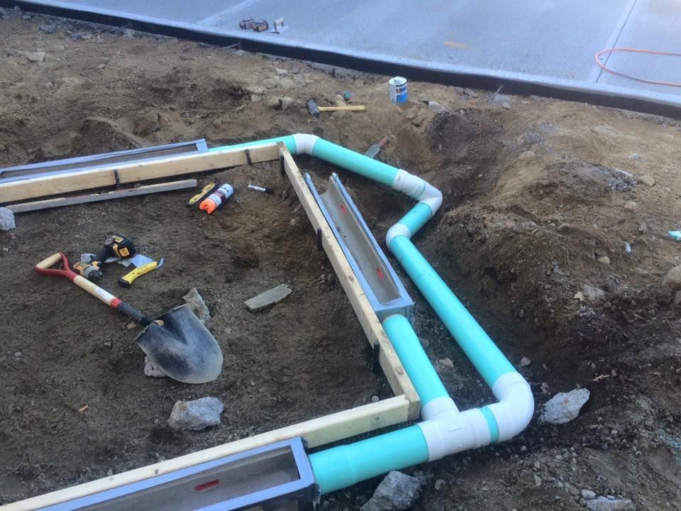 Construction site with drainage system being installed: channels, pipes, shovels, and tools on dirt.