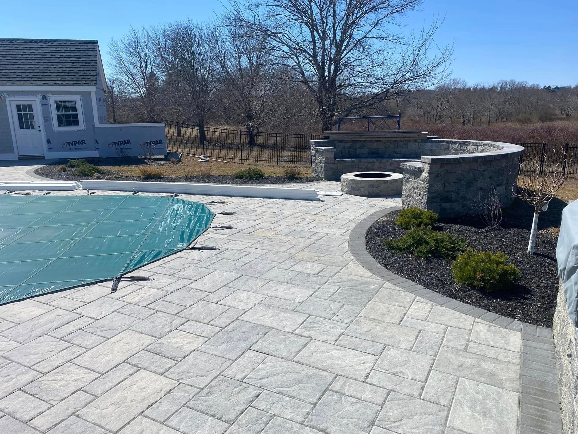 Paver patio with covered pool, fire pit, and stonework seating.