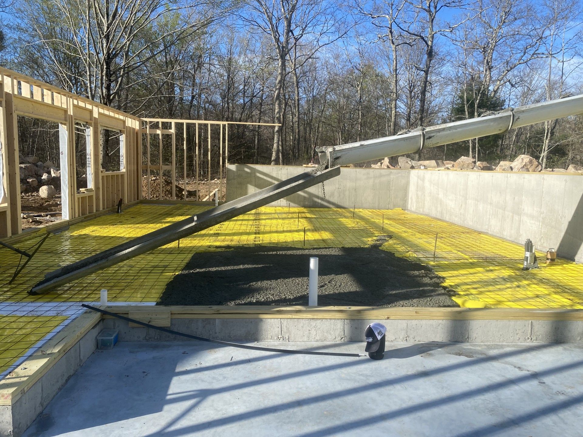 Construction site: Wooden frame, yellow insulation, rebar, concrete foundations, and a chute delivering cement.