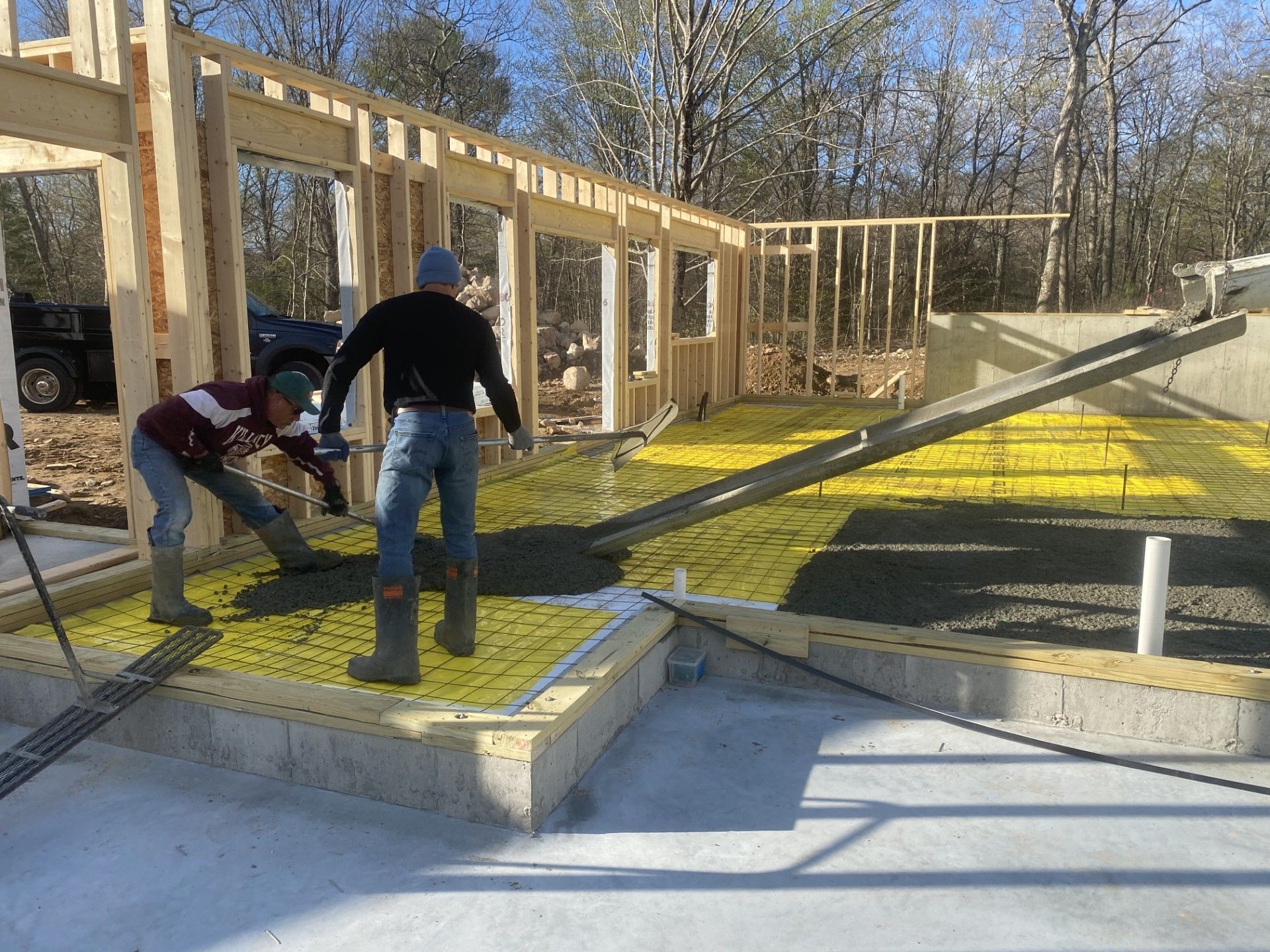 Construction workers installing yellow insulation on a foundation. Wooden frame structure visible.
