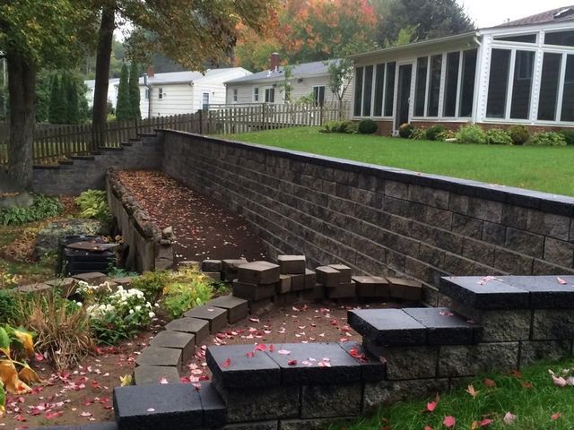 Stone retaining wall with steps, a path, and a lawn in a residential backyard.