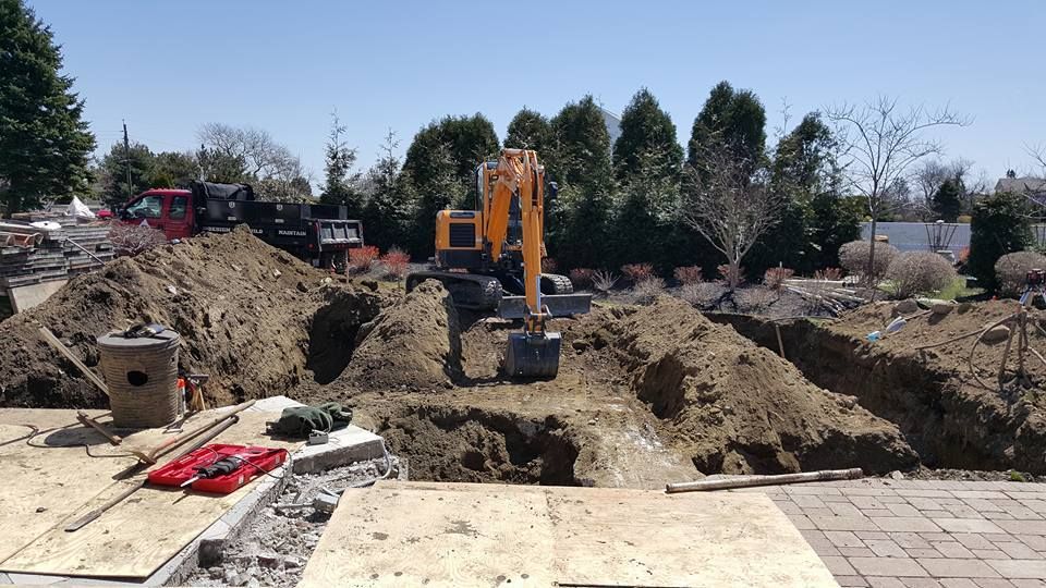 Excavator digging in a construction site with piles of dirt, under a sunny sky.