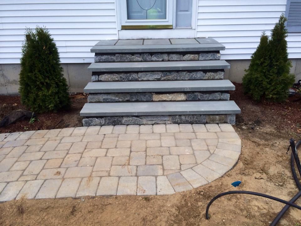 Stone steps leading to a white house with a brick walkway and evergreens on either side.