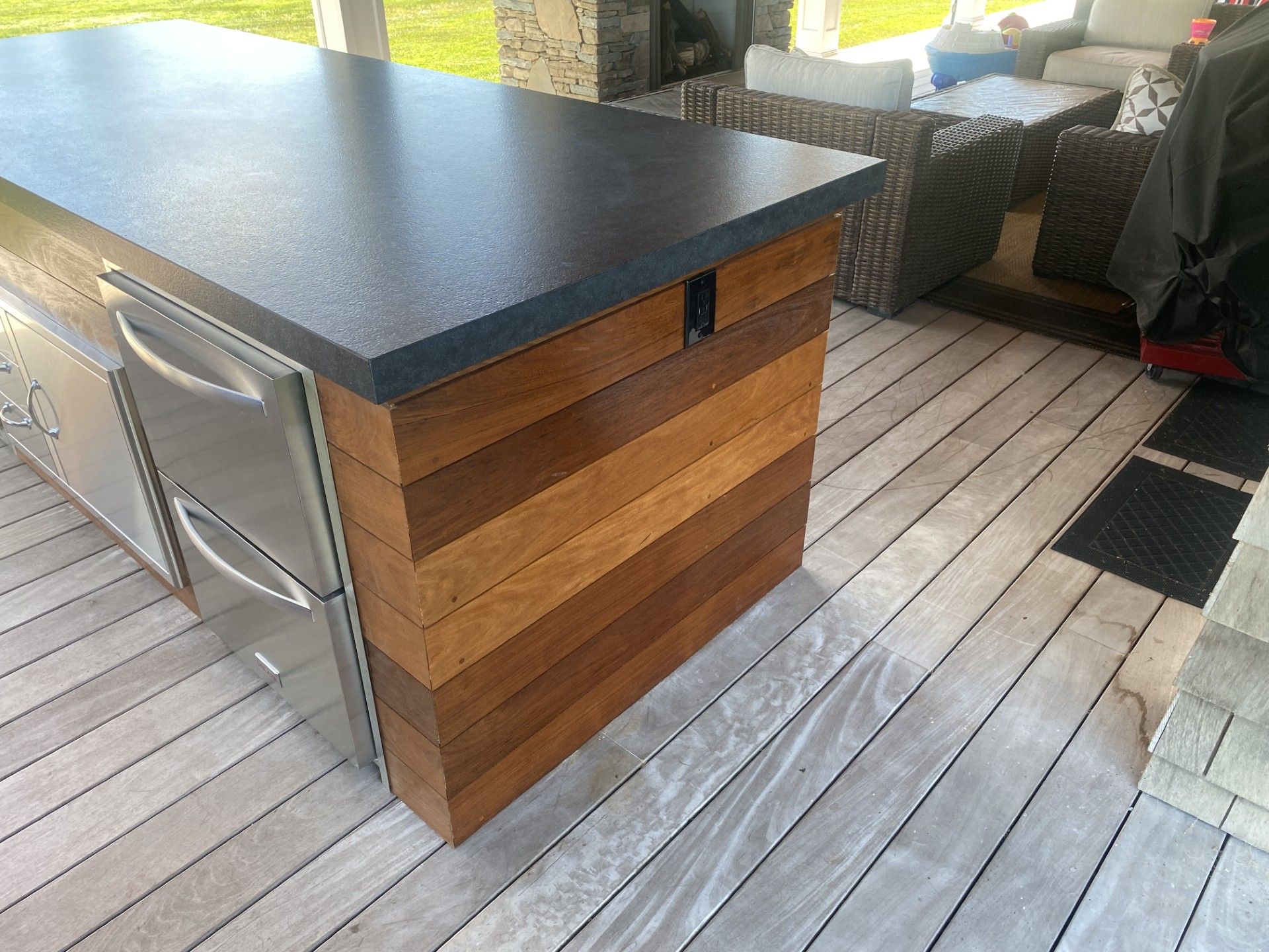 Outdoor kitchen island with a dark countertop and wooden paneling, on a wood deck.
