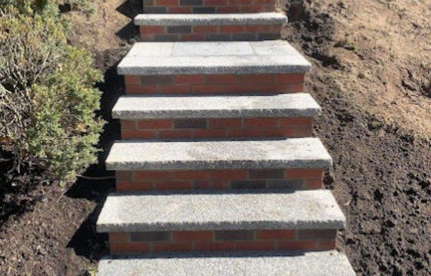 Brick steps with concrete treads ascend a hillside, flanked by soil and shrubbery.